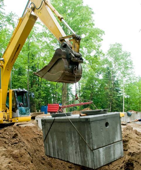 Yellow excavator lifting a concrete container in a wooded construction site