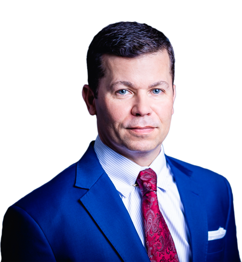 Man in a blue suit, white shirt, and red paisley tie, looking forward, studio portrait.