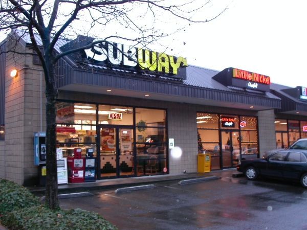 A subway restaurant with a car parked in front of it