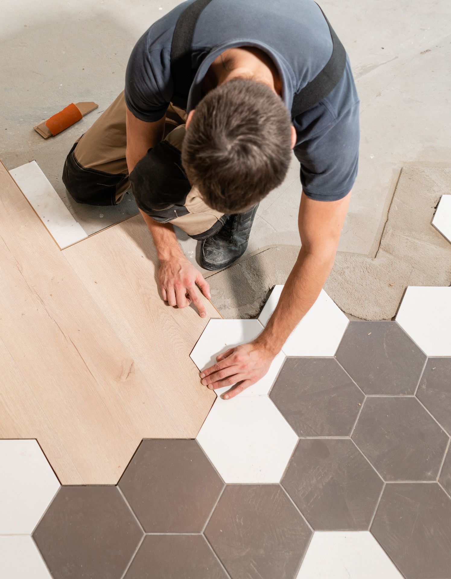 A man is laying tiles on a wooden floor.