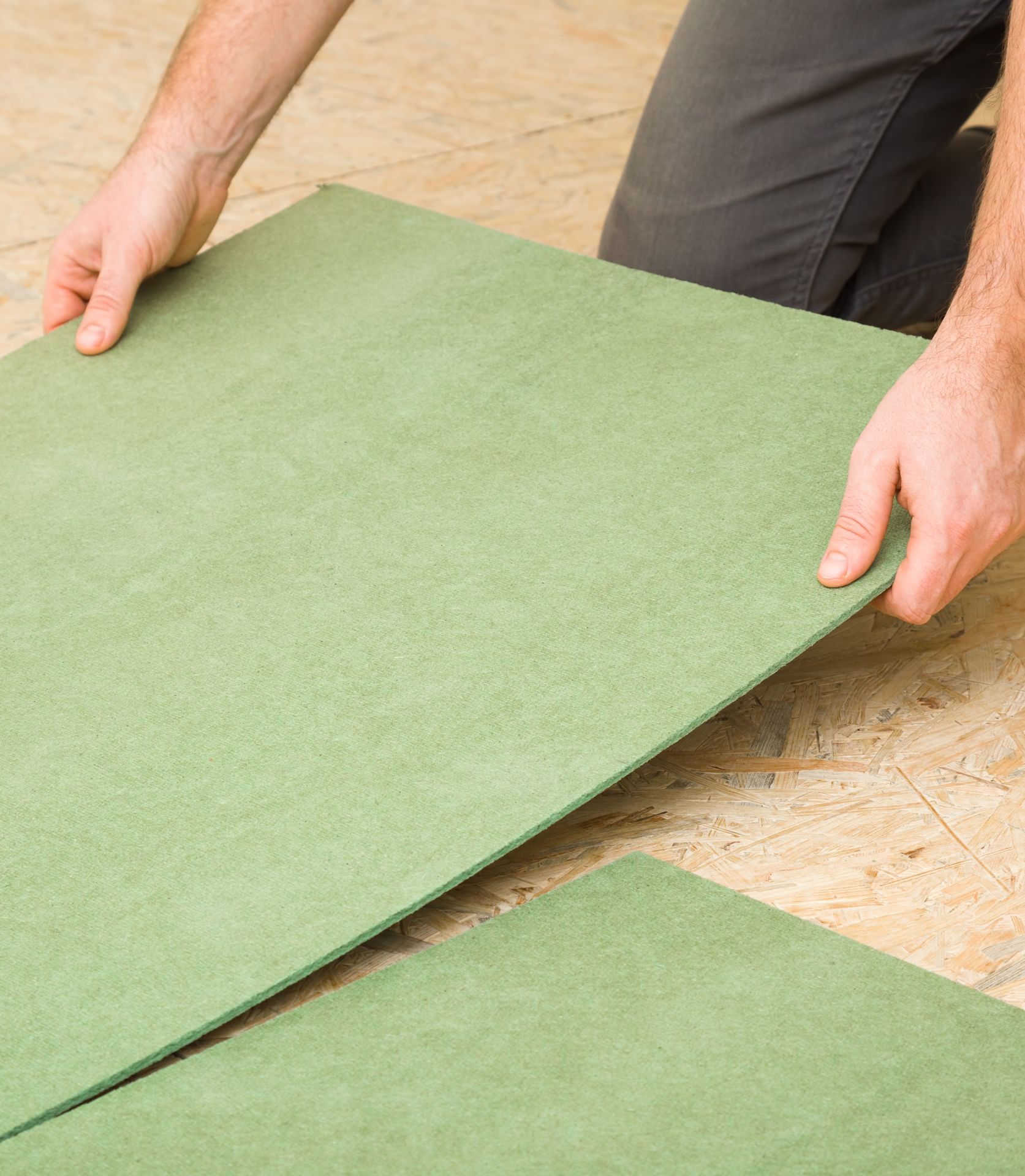 A man is kneeling down holding a piece of green plywood.