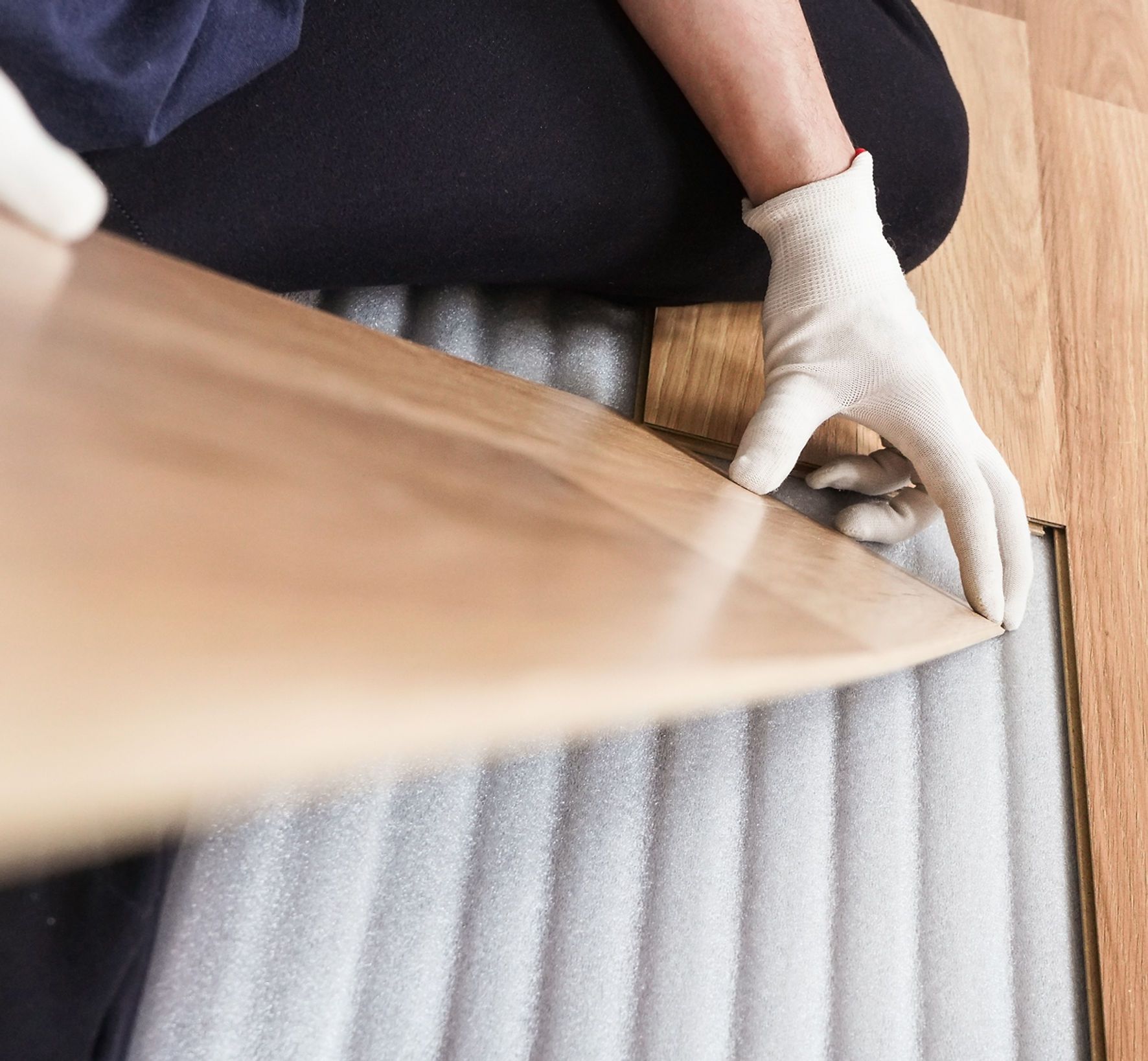 A person wearing white gloves is holding a piece of wood
