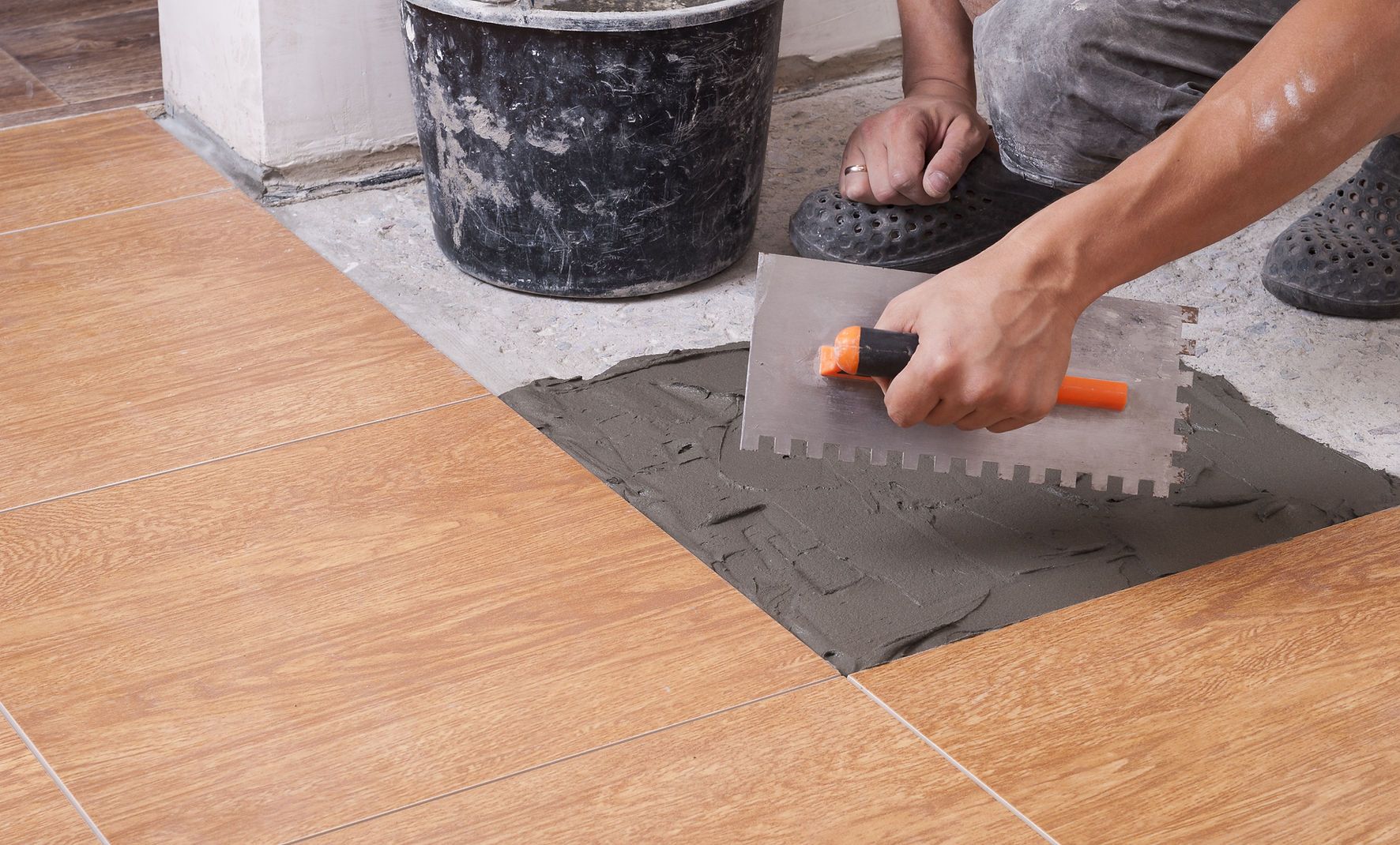A person is laying tiles on a floor with a trowel.