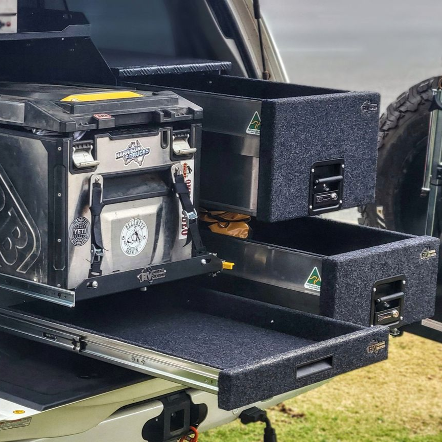Open drawers in the back of a black SUV, filled with gear. Spare tire visible, outdoor setting.