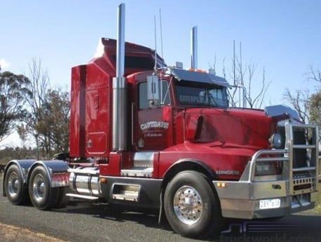 Red semi-truck with chrome accents and a front bumper guard, parked on a road, blue sky.