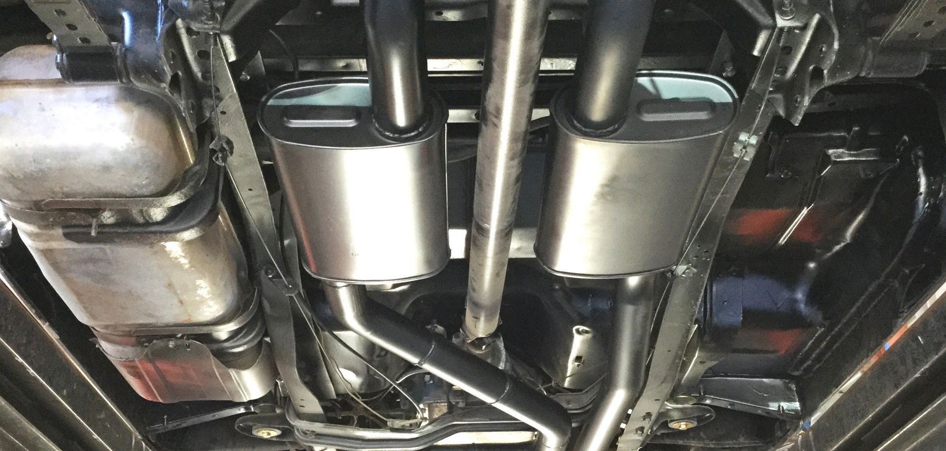 Undercarriage view of a car's exhaust system with mufflers, pipes, and catalytic converters.