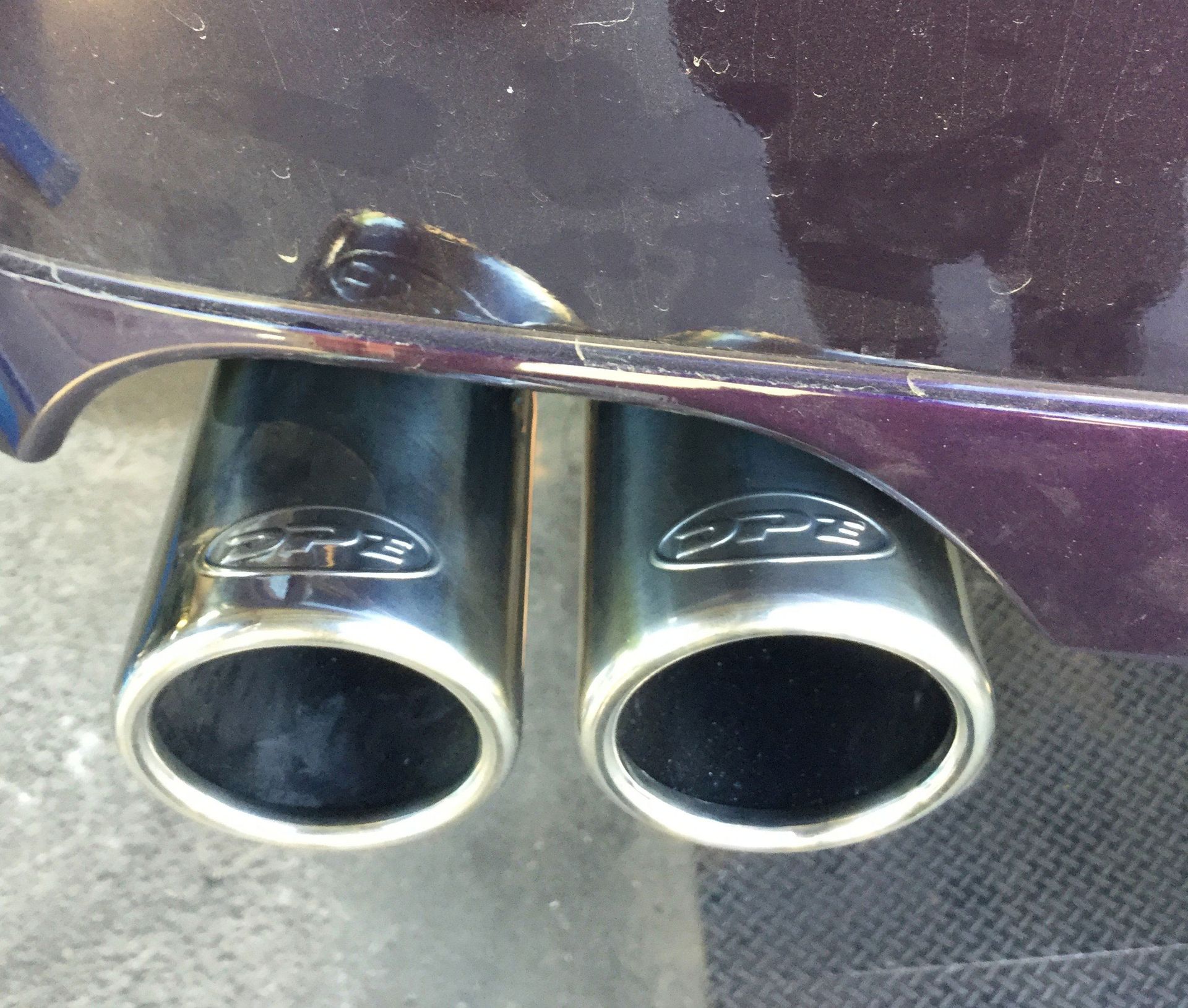 Two black exhaust pipes with a logo, on a purple car.