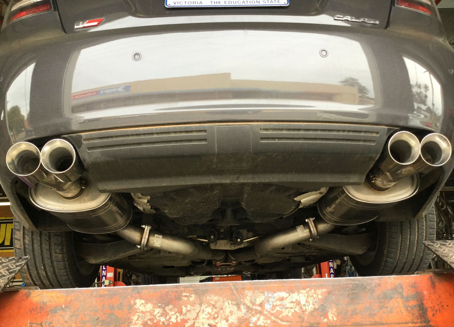 Grey car's underside on a lift, showing its dual exhaust pipes and mufflers.
