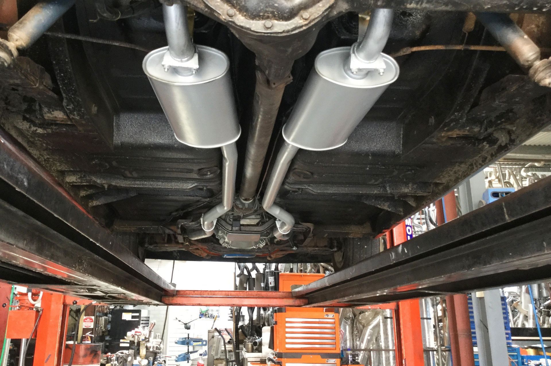 Underside of a vehicle with a new dual exhaust system in a garage.