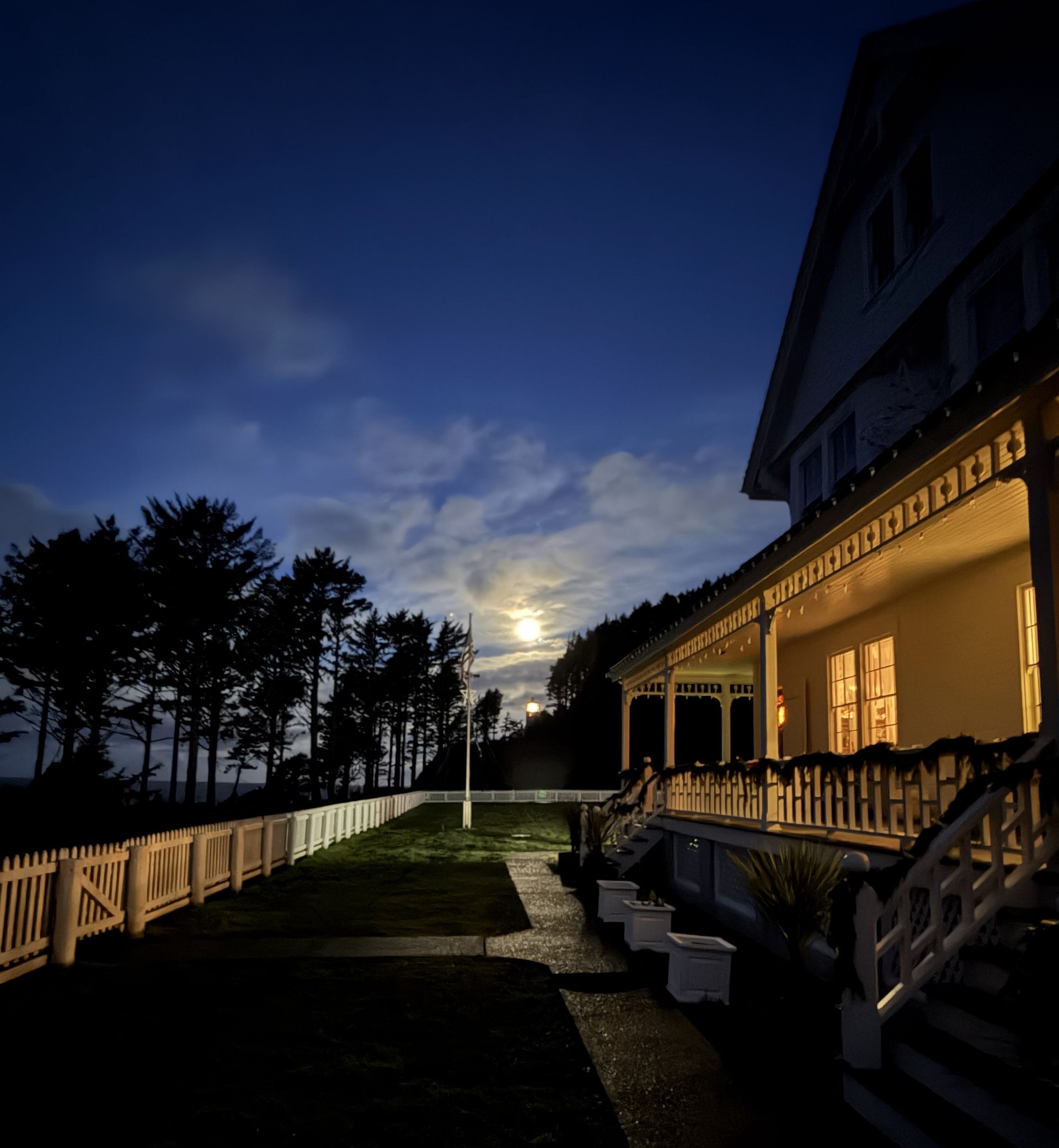 Night view of a white house with a porch and lit windows; moonlit sky.