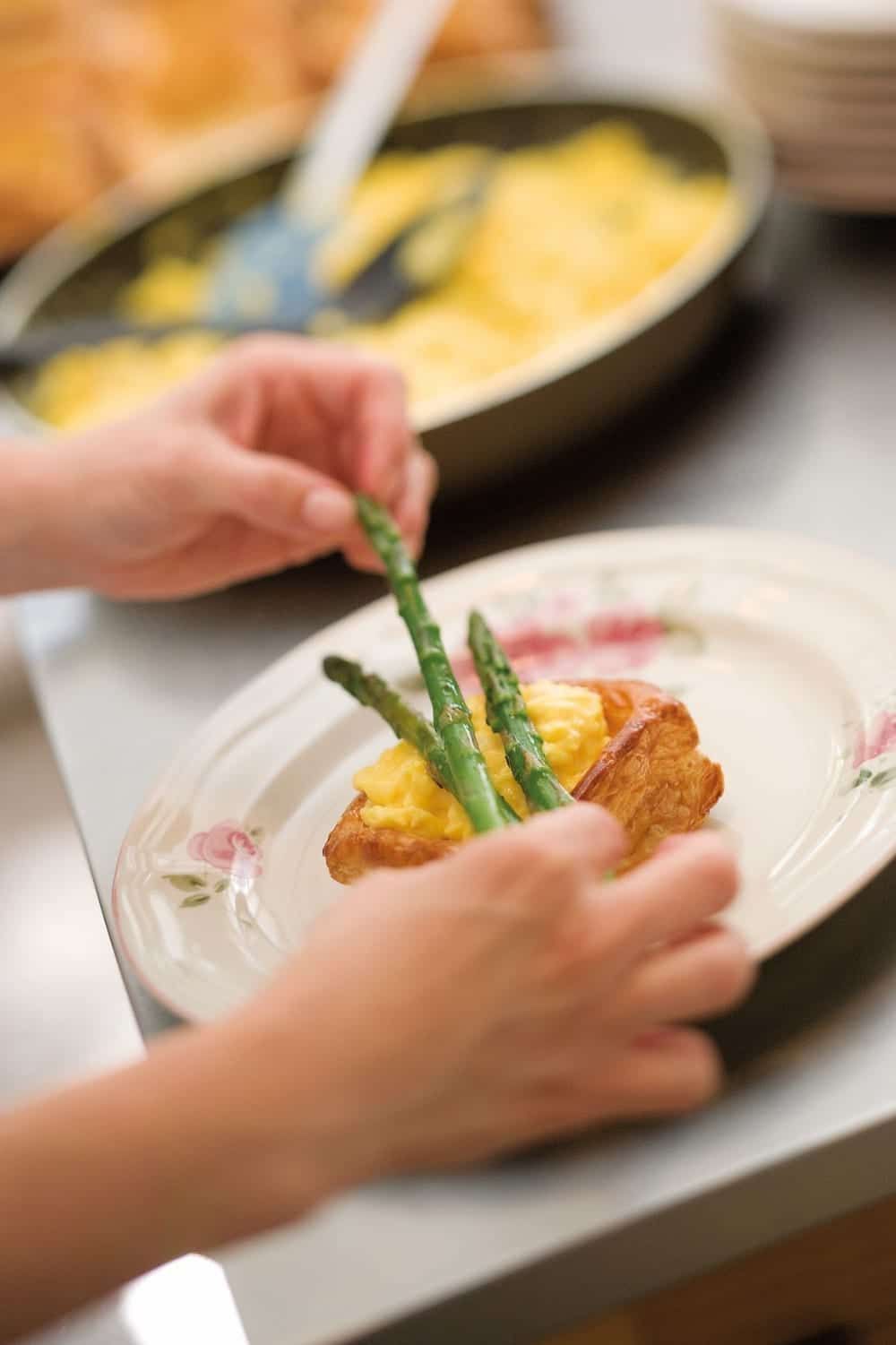 A person is putting asparagus on a plate of food