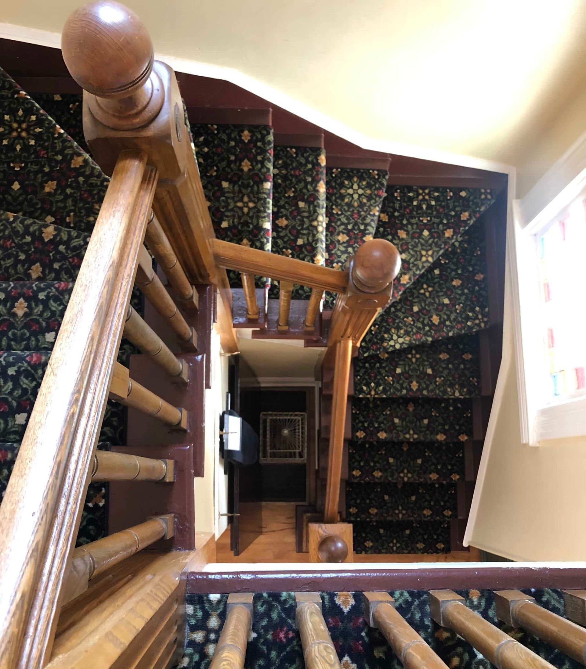 Overhead view of a staircase with patterned carpet and wooden railings.