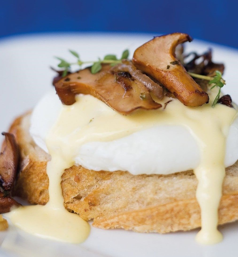 A close up of a sandwich with eggs and mushrooms on a plate