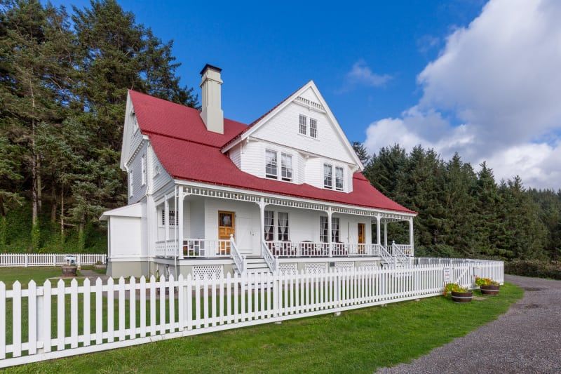 A large white house with a red roof and a white picket fence surrounding it.