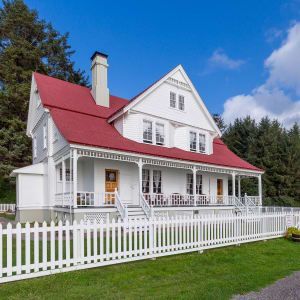 A white house with a red roof and a white picket fence surrounding it.