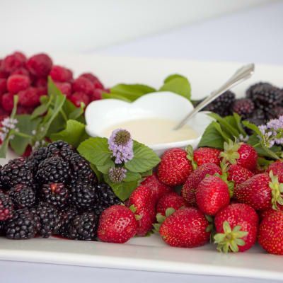 A white plate topped with strawberries , blackberries , raspberries and a bowl of dipping sauce.