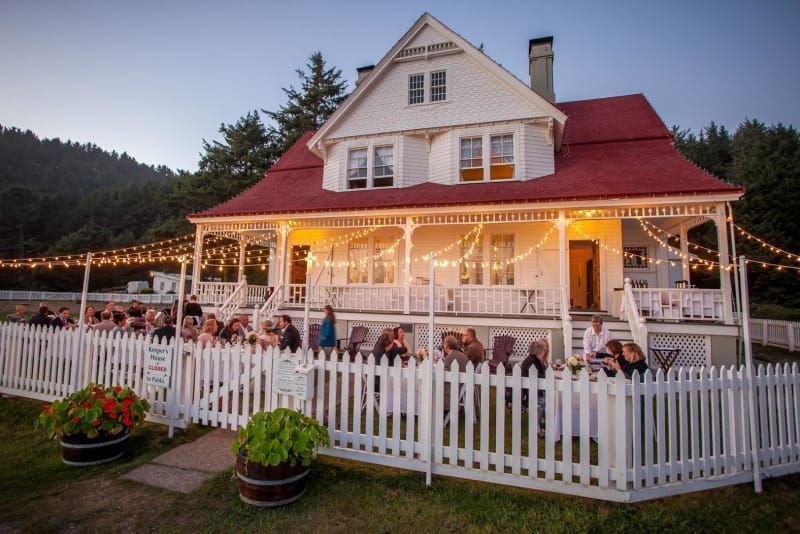 A group of people are sitting on the porch of a house behind a white picket fence.