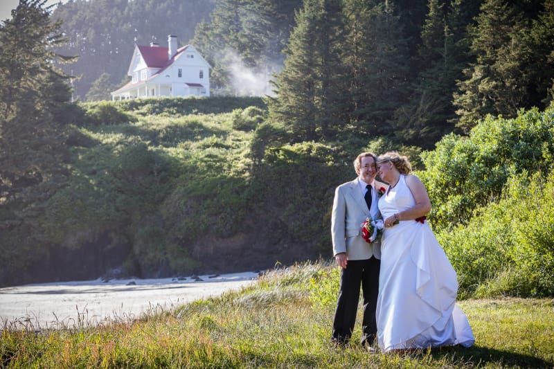 A bride and groom are posing for a picture in front of a house on a hill.