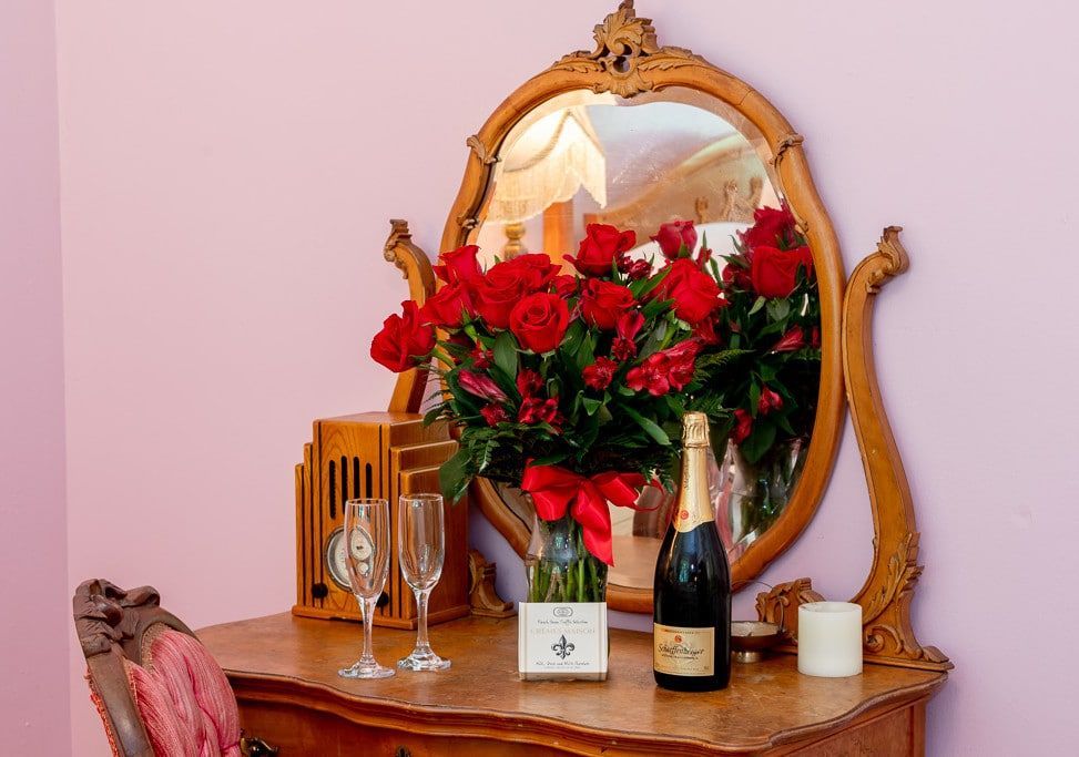A dresser with a vase of red roses and a bottle of champagne
