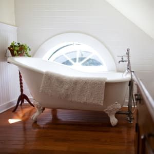 A bathtub with claw feet is in a bathroom next to a window.