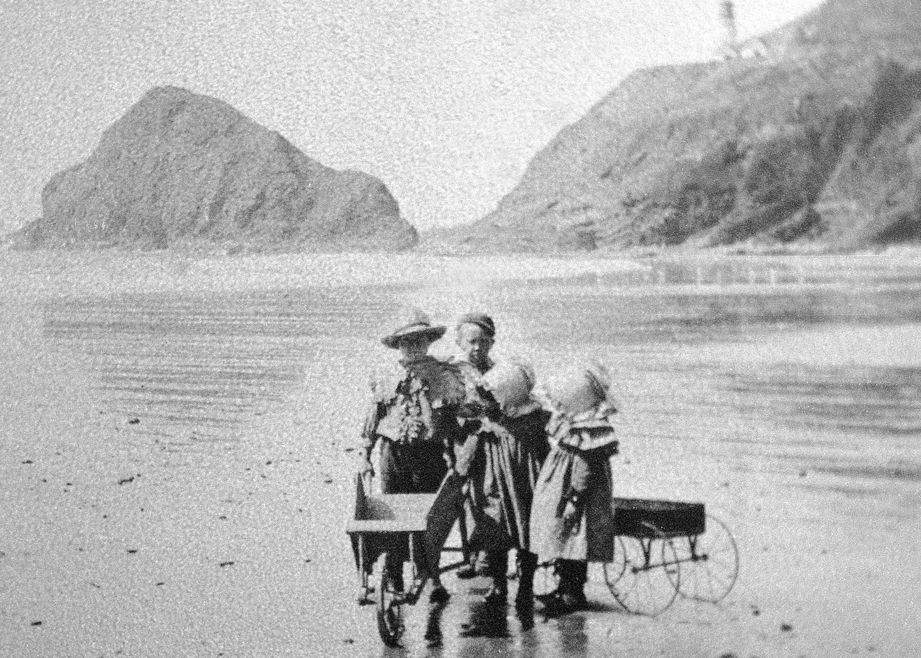 A black and white photo of two people in a wheelchair on a beach.