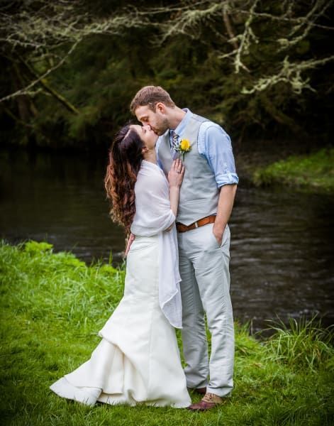 A bride and groom are kissing in front of a river.