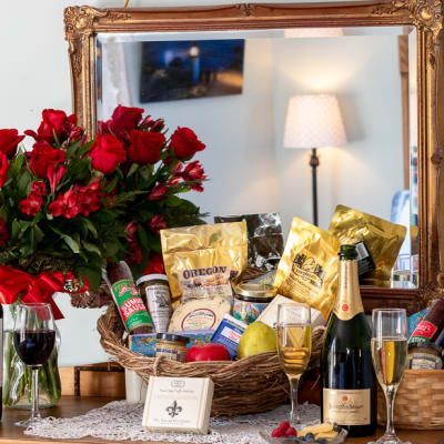 A basket of food and a bottle of champagne are on a table in front of a mirror.