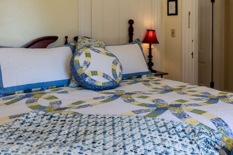 A bed with a quilt and pillows in a bedroom with a lamp.