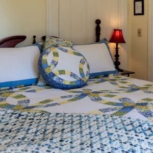 A bed with a quilt and pillows in a bedroom with a lamp.