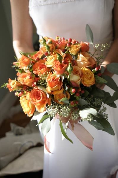 A woman in a white dress is holding a bouquet of orange and yellow flowers