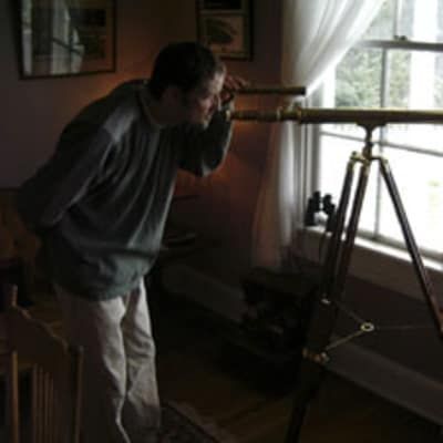 A man looking through a telescope in front of a window