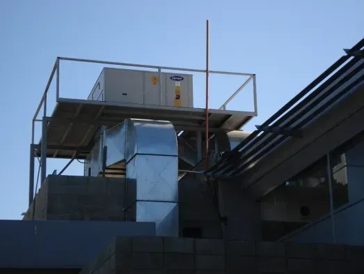 Unidad de climatización en la azotea y conductos metálicos en un edificio en construcción al anochecer.