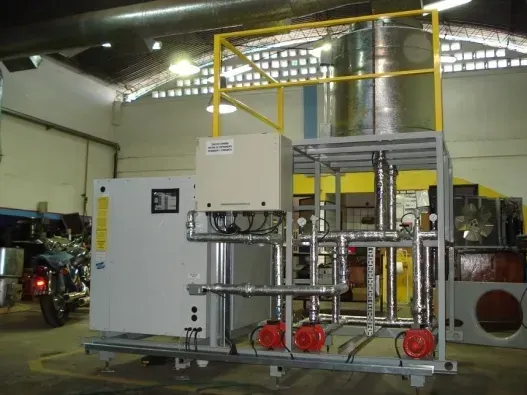 Gran máquina industrial con tuberías metálicas y componentes rojos dentro de un taller de fábrica.