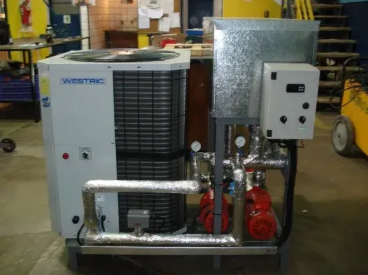 Unidad de climatización industrial con compresor, tuberías metálicas y caja de control en un taller.