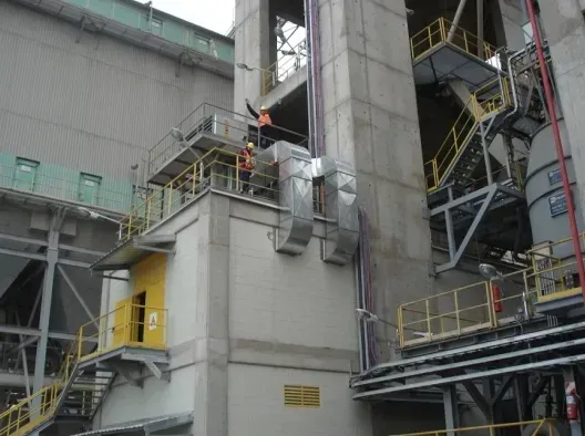 Instalación industrial con pasarelas metálicas, tuberías y un trabajador vestido de naranja sobre una plataforma.