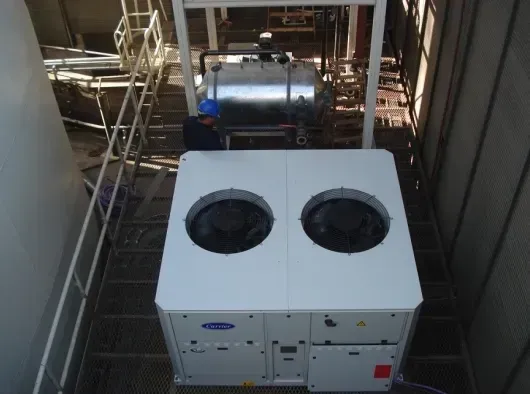 Dos grandes unidades de climatización instaladas en la azotea de un espacio industrial estrecho, vistas desde arriba.