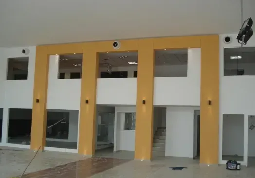 Interior con grandes aberturas en las paredes y ventanas con marcos amarillos en una habitación prácticamente vacía.