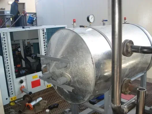 Gran cámara industrial metálica en un laboratorio, con maquinaria y tuberías a su alrededor.