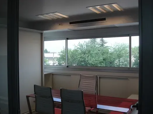 Sala de conferencias con mesa, sillas y una gran ventana con vistas a los árboles.