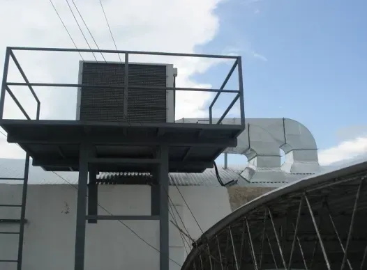 Unidad de climatización en la azotea y barandilla metálica en la plataforma de un edificio contra un cielo azul.