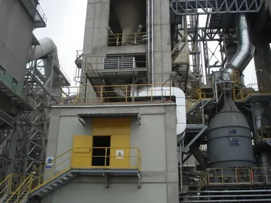 Instalación industrial con torres metálicas, tuberías y una puerta de carga amarilla en un edificio gris.