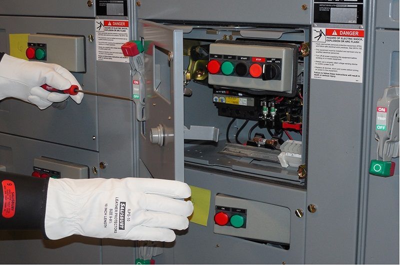 Person in safety gloves using a tool inside an open electrical panel.