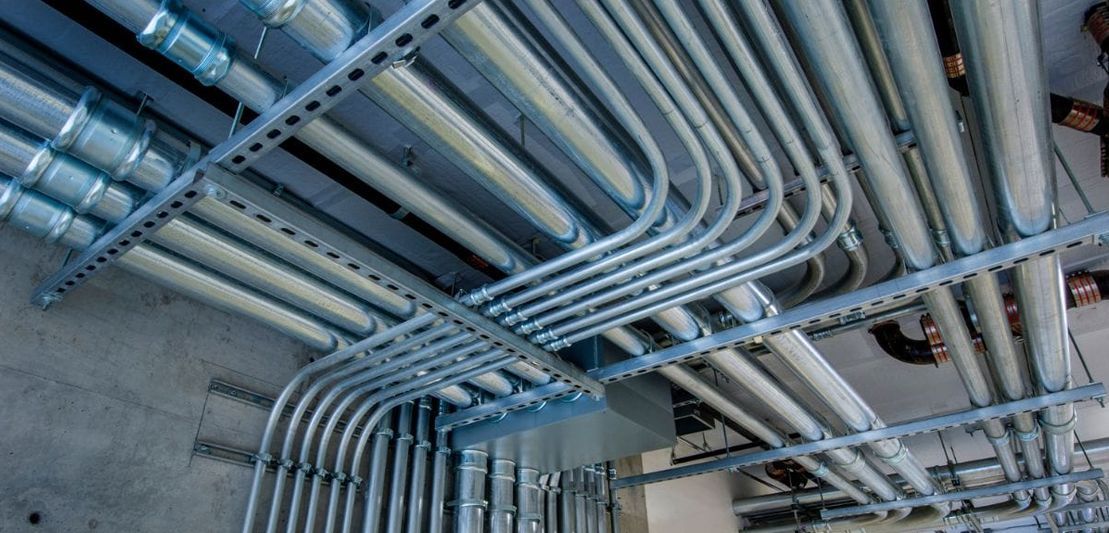 Metal pipes and conduits attached to the ceiling of a building.