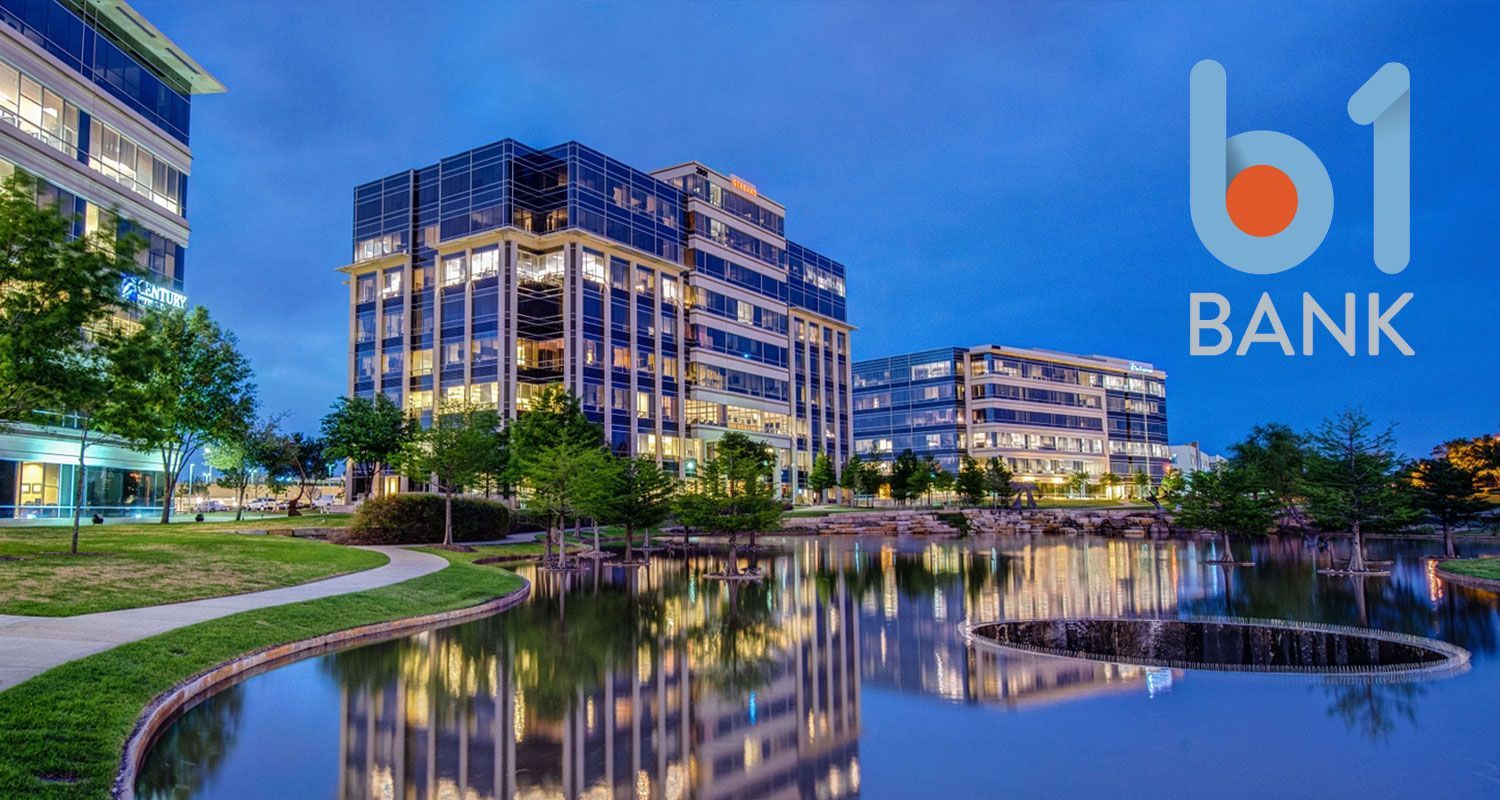 Modern office buildings with a reflective pond, b1BANK logo in the sky.