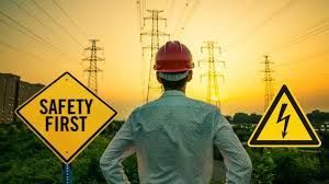 Worker in a hard hat stands before power lines at sunset, with safety signs that read,