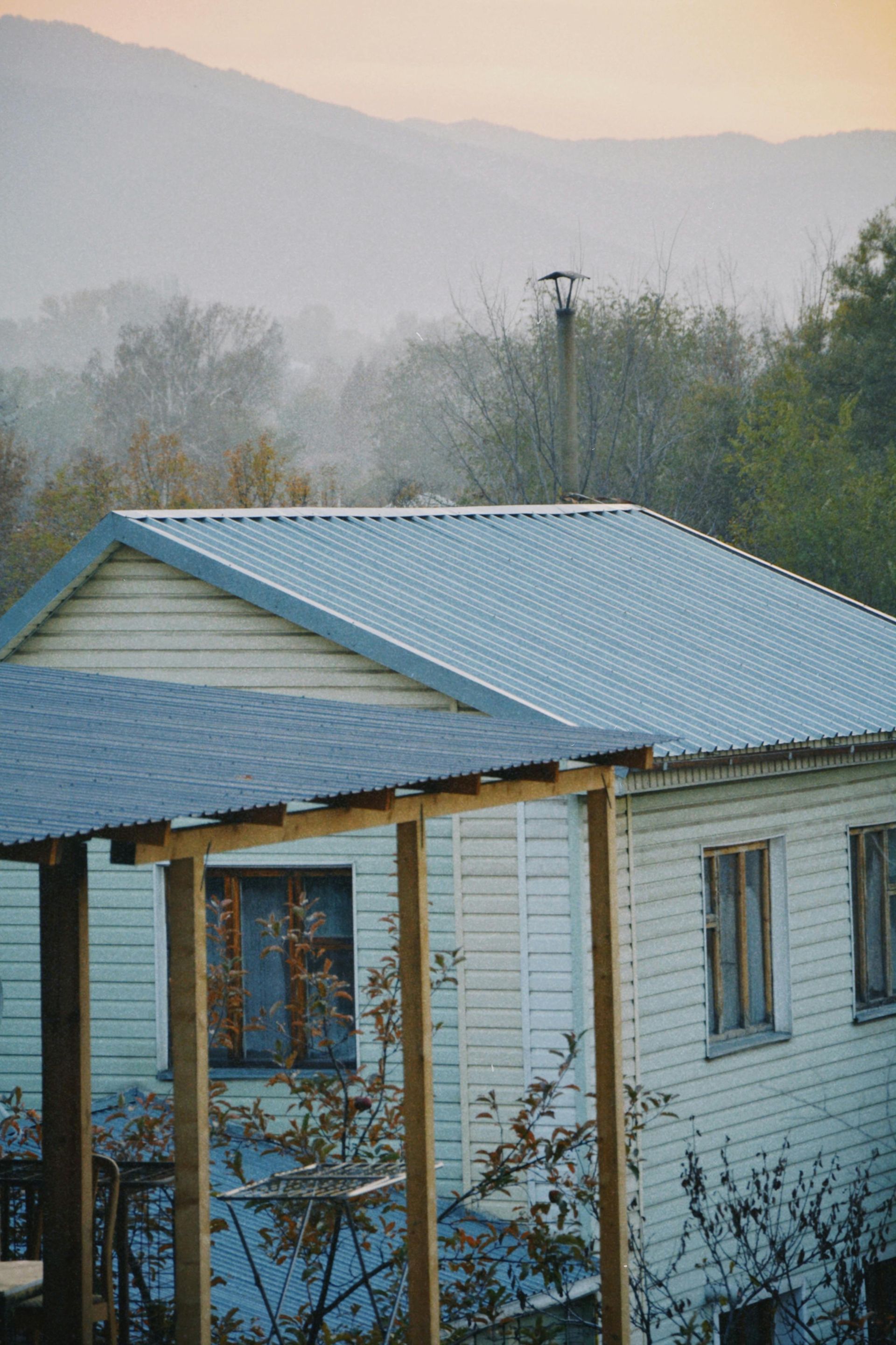 Small white house with a blue metal roof in a misty wooded landscape at dawn