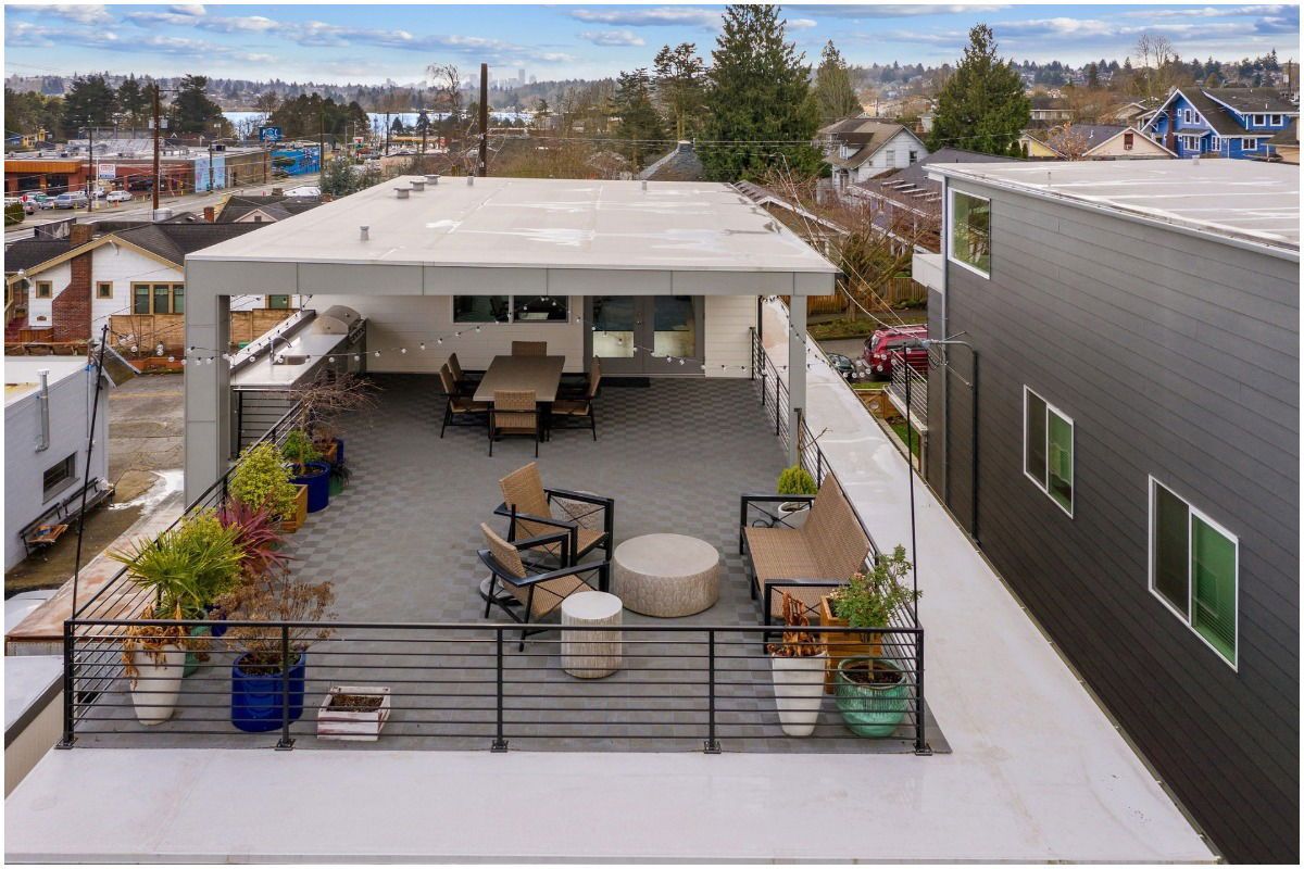 Rooftop deck with seating and dining area; gray flooring, metal railing, city view.
