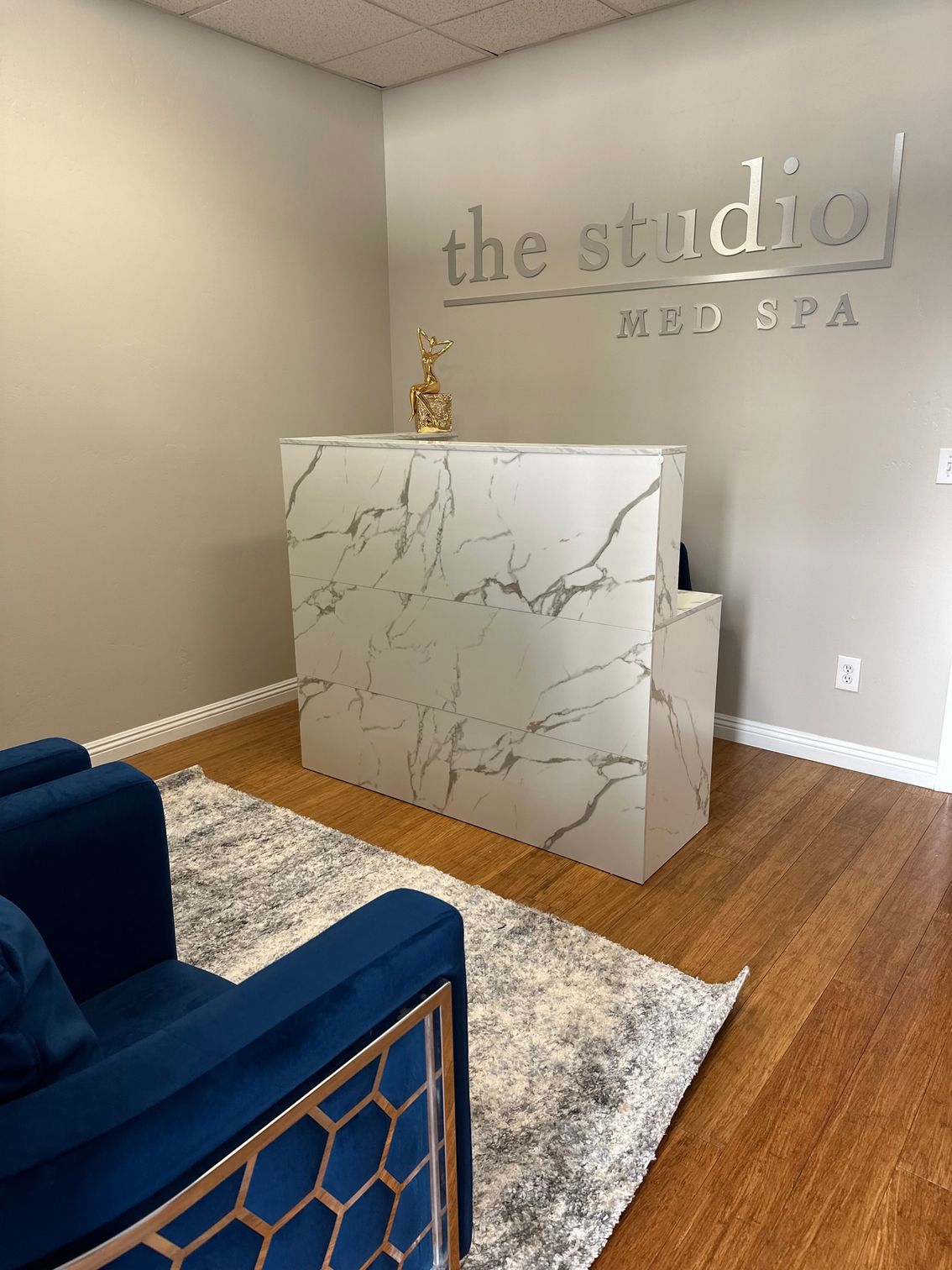 Spa reception desk in a small lobby with beige walls, navy chair, and marble-patterned counter.
