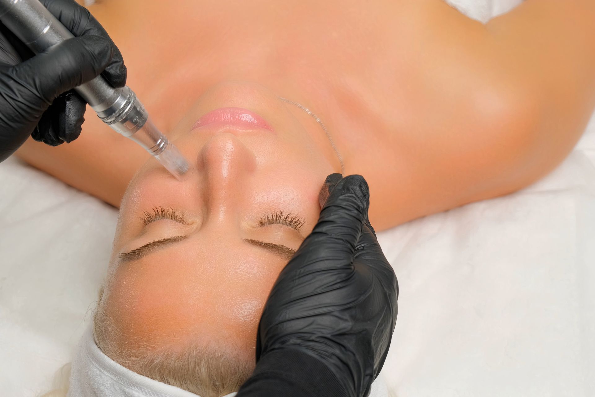 Gloved hands using a syringe on a woman’s nose during a cosmetic facial treatment