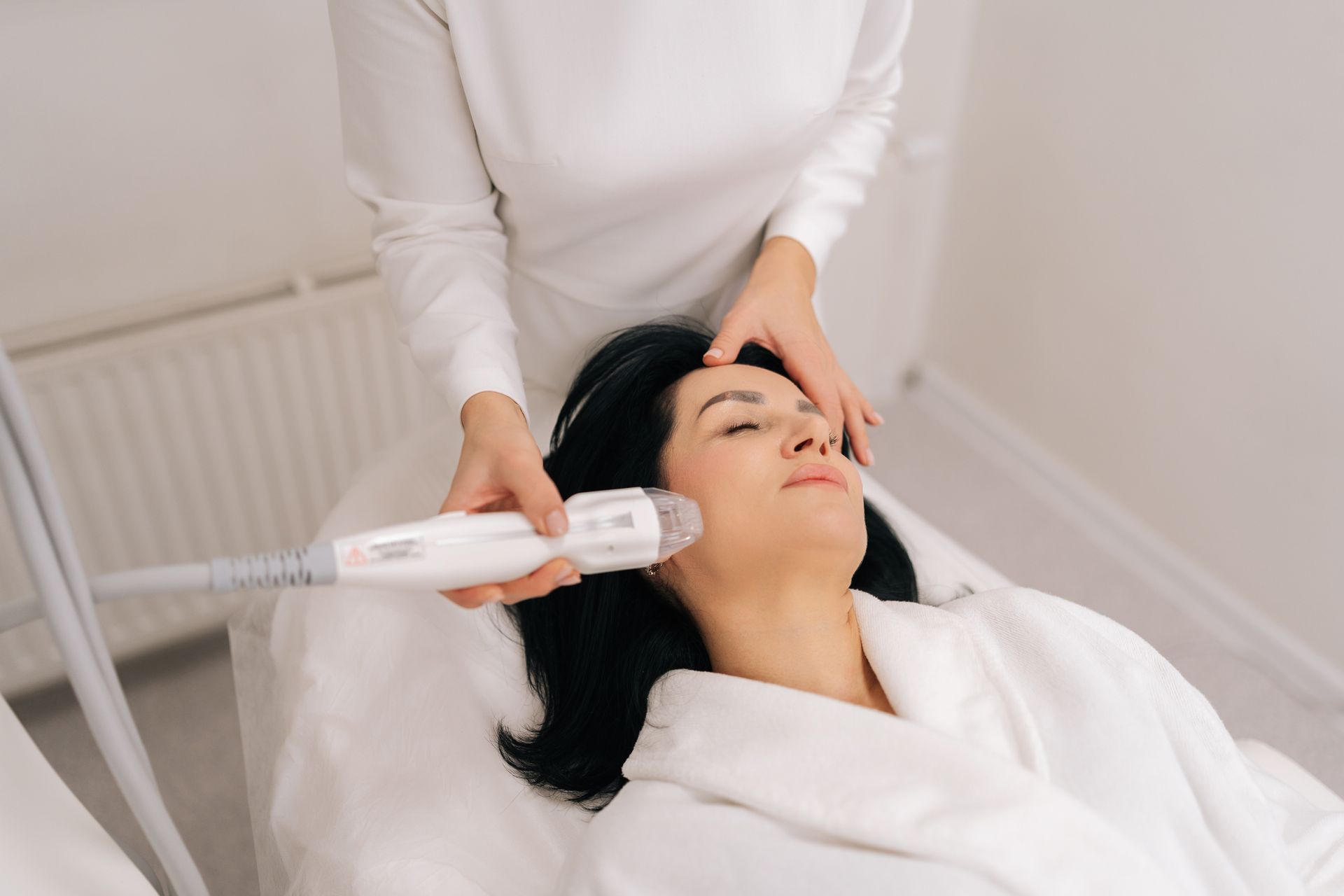 Facial treatment with a handheld device at a spa, woman lying back in a robe